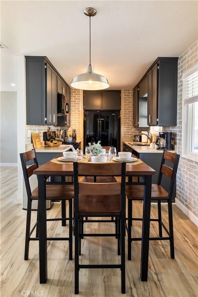 kitchen with sink, black appliances, brick wall, decorative light fixtures, and light wood-type flooring