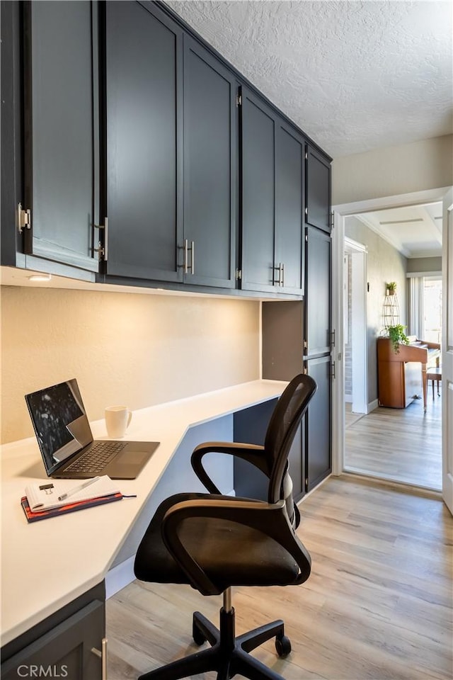 office area with built in desk, light hardwood / wood-style floors, and a textured ceiling