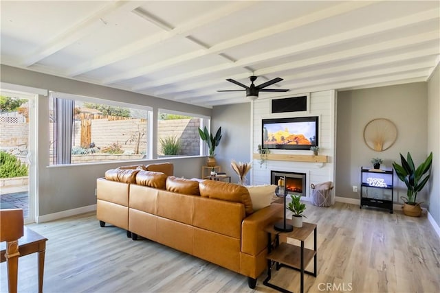 living room featuring light hardwood / wood-style flooring, ceiling fan, a fireplace, and beamed ceiling