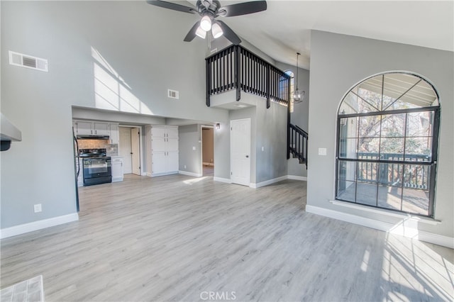 unfurnished living room with ceiling fan, light wood-type flooring, and a towering ceiling