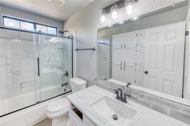 full bathroom featuring bath / shower combo with glass door, vanity, a textured ceiling, and toilet