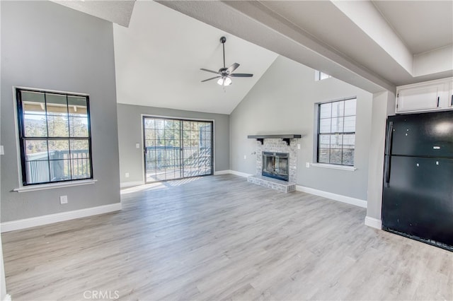 unfurnished living room with ceiling fan, a stone fireplace, a high ceiling, and light wood-type flooring