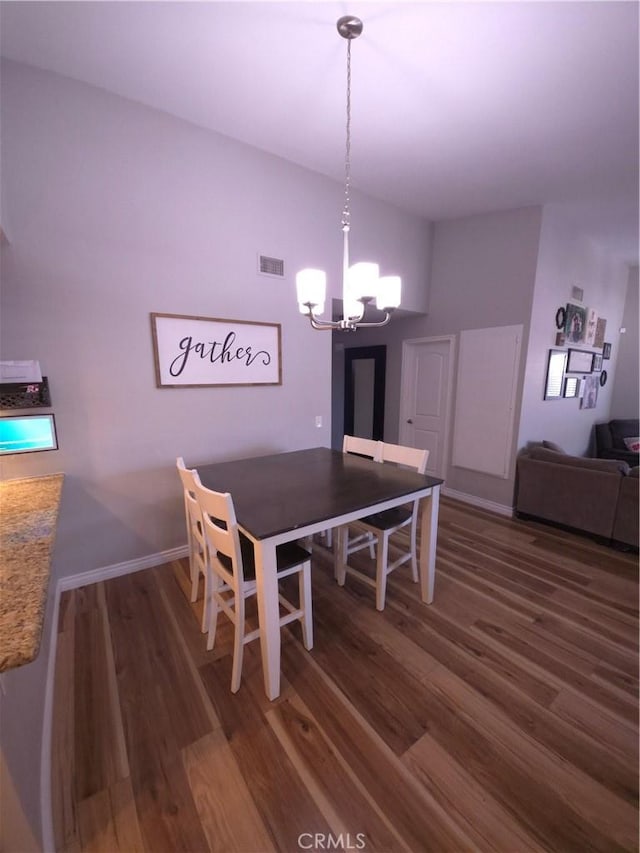 dining room featuring dark hardwood / wood-style flooring, vaulted ceiling, and an inviting chandelier