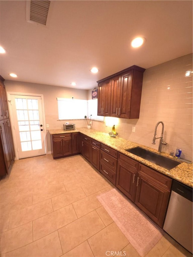 kitchen with stainless steel dishwasher, light stone countertops, sink, and light tile patterned floors