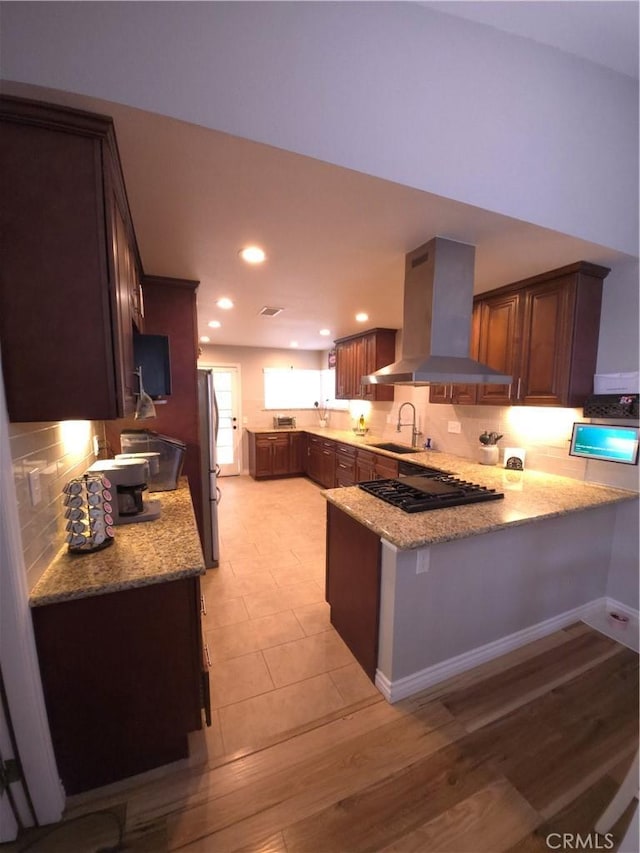 kitchen with sink, stainless steel refrigerator, light stone counters, island range hood, and kitchen peninsula