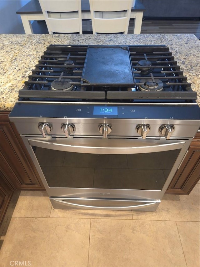 interior details featuring stainless steel gas range oven, dark brown cabinets, and light stone counters