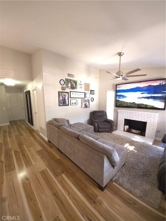 living room with a brick fireplace, ceiling fan, and light hardwood / wood-style flooring