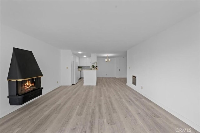 unfurnished living room with an inviting chandelier, light hardwood / wood-style flooring, and heating unit