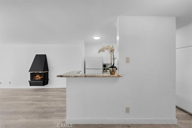 kitchen featuring white refrigerator, light stone countertops, light wood-type flooring, and kitchen peninsula