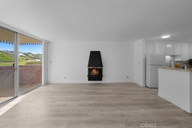 unfurnished living room featuring floor to ceiling windows, sink, and light hardwood / wood-style flooring