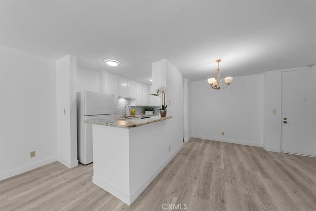 kitchen featuring pendant lighting, backsplash, white refrigerator, white cabinets, and kitchen peninsula