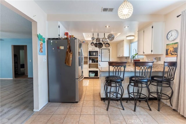 kitchen with stainless steel fridge, stone counters, black microwave, white cabinets, and kitchen peninsula