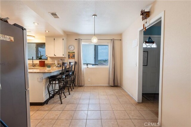 kitchen with white cabinetry, stainless steel fridge, hanging light fixtures, light tile patterned floors, and light stone countertops