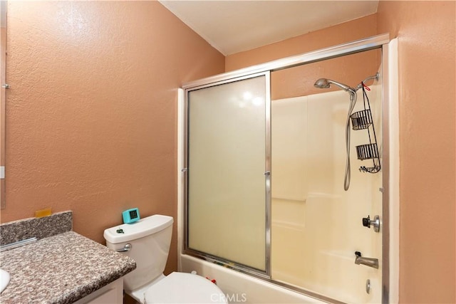 bathroom featuring combined bath / shower with glass door, toilet, vanity, and a textured wall