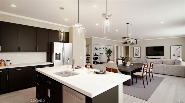 kitchen featuring sink, crown molding, pendant lighting, stainless steel appliances, and a kitchen island with sink