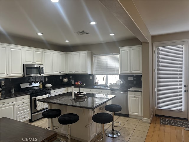 kitchen with light tile patterned floors, appliances with stainless steel finishes, white cabinetry, a center island, and a kitchen bar