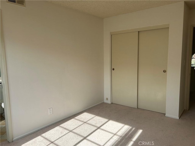 unfurnished bedroom with light carpet, a closet, and a textured ceiling