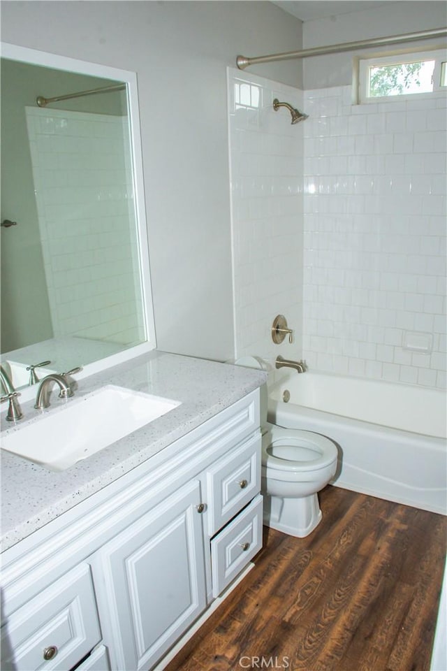 full bathroom with hardwood / wood-style flooring, vanity, tiled shower / bath combo, and toilet