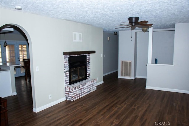 unfurnished living room with dark hardwood / wood-style floors, ceiling fan, a brick fireplace, and a textured ceiling