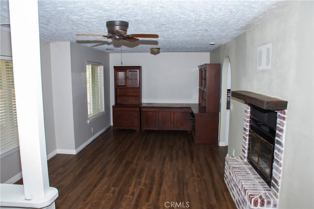 unfurnished living room with ceiling fan, dark wood-type flooring, a fireplace, and a textured ceiling