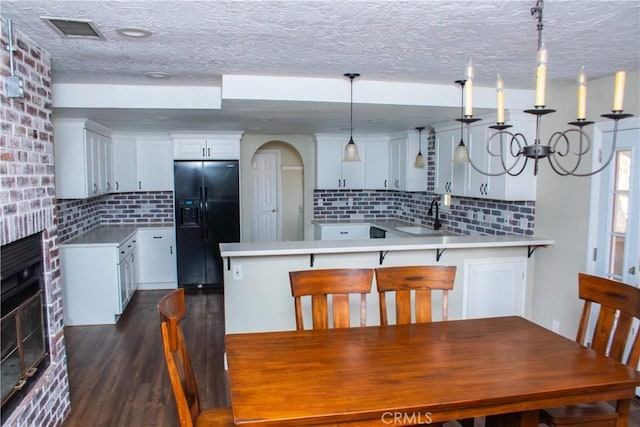 kitchen with pendant lighting, white cabinetry, a breakfast bar area, black fridge with ice dispenser, and kitchen peninsula