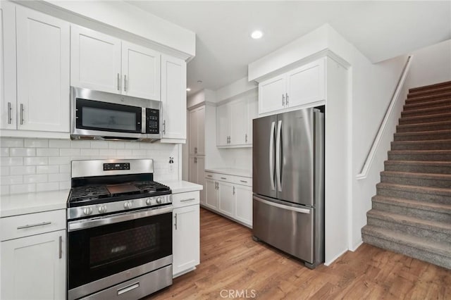 kitchen featuring tasteful backsplash, stainless steel appliances, white cabinets, and light wood-type flooring