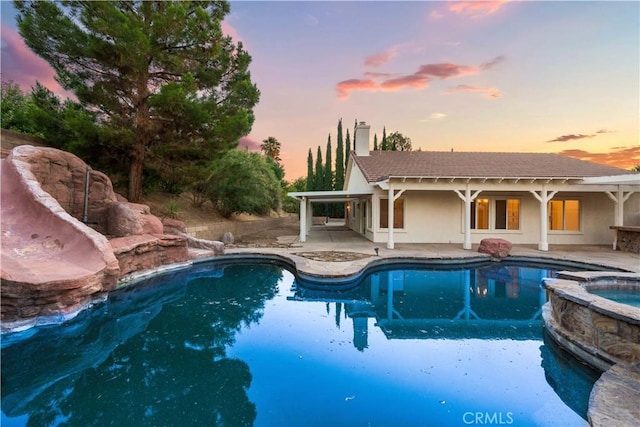 pool at dusk featuring a patio and an in ground hot tub