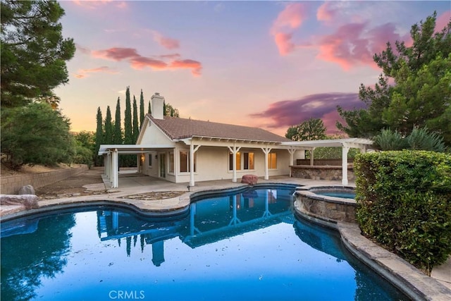 pool at dusk featuring an in ground hot tub and a patio