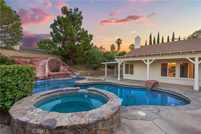 pool at dusk featuring an in ground hot tub and a patio area