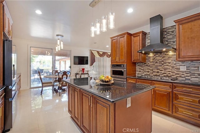 kitchen featuring appliances with stainless steel finishes, decorative light fixtures, dark stone counters, a center island, and wall chimney range hood