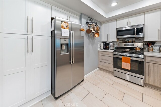 kitchen featuring light brown cabinetry, tasteful backsplash, white cabinetry, light tile patterned floors, and stainless steel appliances