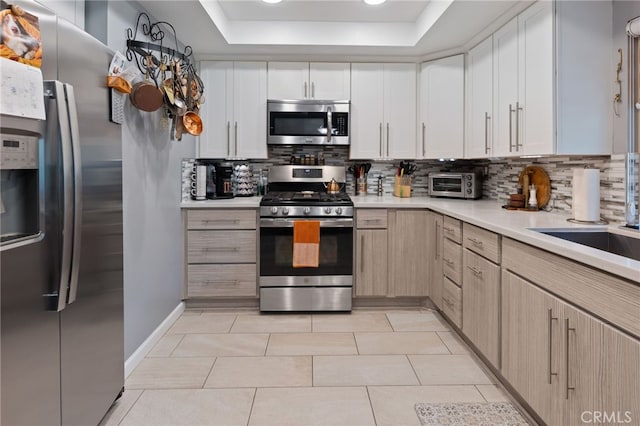 kitchen featuring light brown cabinetry, tasteful backsplash, light tile patterned floors, a tray ceiling, and stainless steel appliances