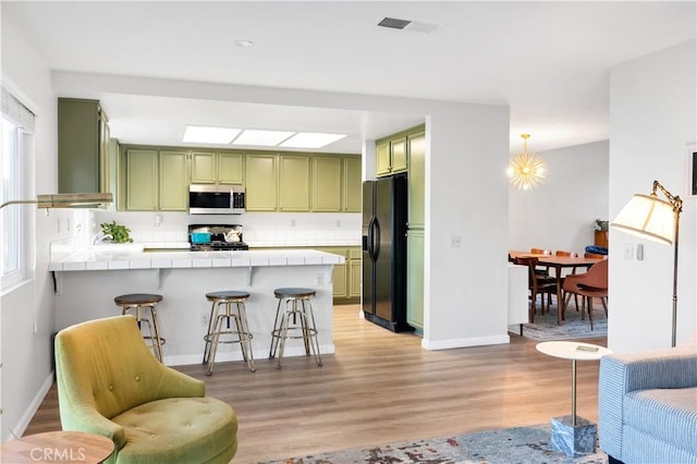 kitchen featuring a breakfast bar, tile countertops, appliances with stainless steel finishes, kitchen peninsula, and green cabinets