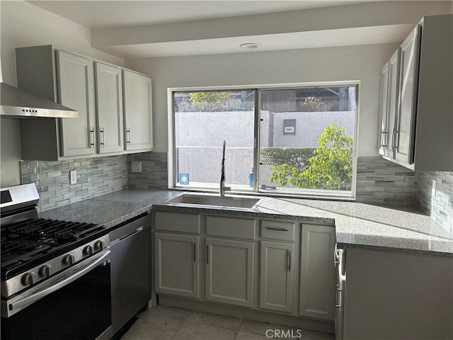 kitchen with sink, gray cabinets, appliances with stainless steel finishes, tasteful backsplash, and wall chimney exhaust hood