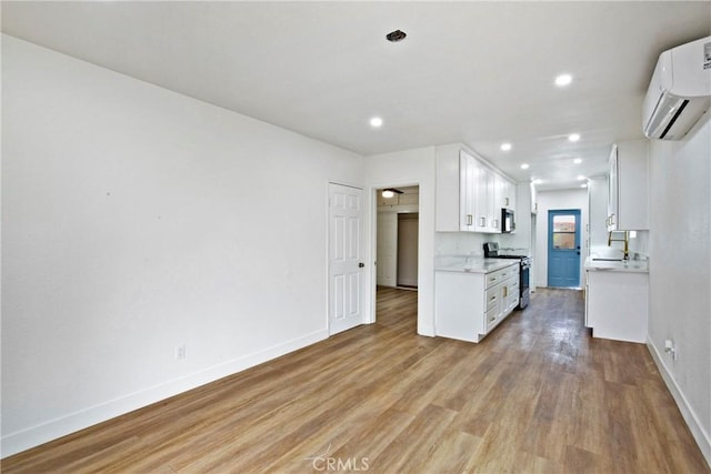 kitchen with stainless steel appliances, white cabinets, a wall unit AC, and light hardwood / wood-style floors