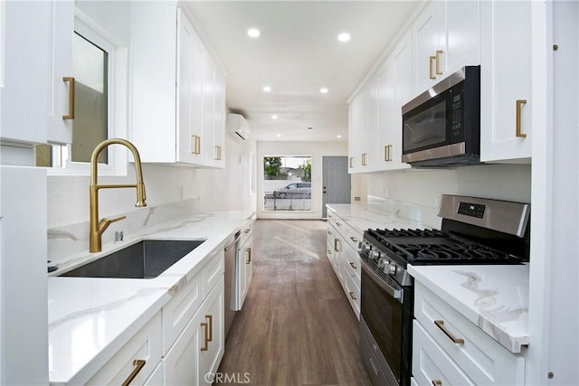 kitchen with sink, appliances with stainless steel finishes, white cabinetry, light stone countertops, and an AC wall unit