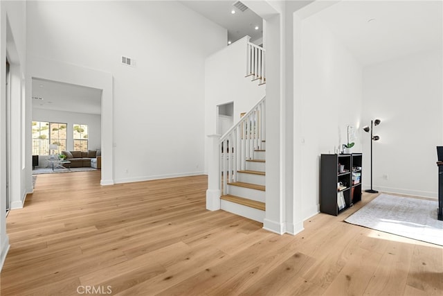 stairs featuring visible vents, a high ceiling, baseboards, and wood finished floors