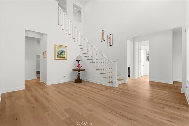 interior space featuring stairs, light wood finished floors, a towering ceiling, and baseboards