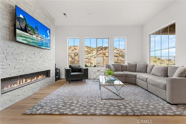 living room featuring a wealth of natural light, visible vents, wood finished floors, and a stone fireplace