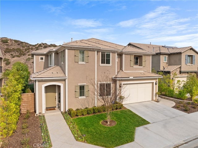 view of front of home with an attached garage, concrete driveway, a tiled roof, stucco siding, and a front lawn