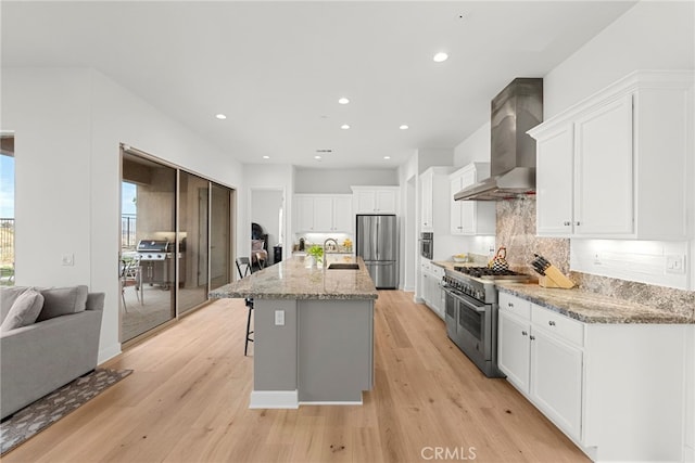 kitchen with stainless steel appliances, a sink, white cabinetry, wall chimney exhaust hood, and an island with sink