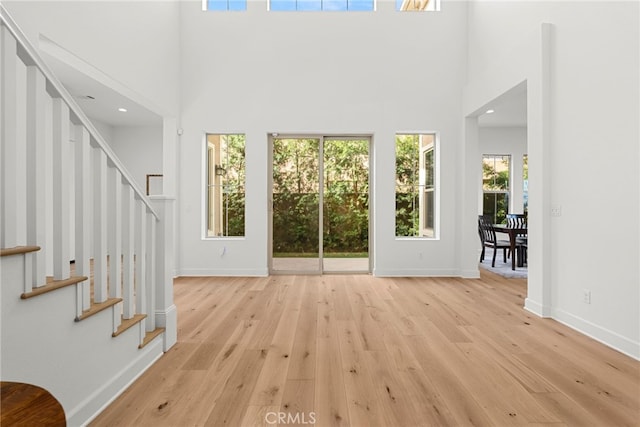 foyer with light wood-style flooring, a high ceiling, stairway, and baseboards