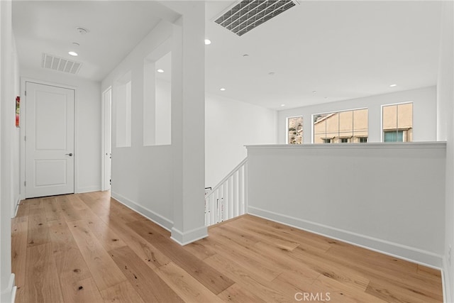 hall with light wood-style floors, visible vents, and an upstairs landing