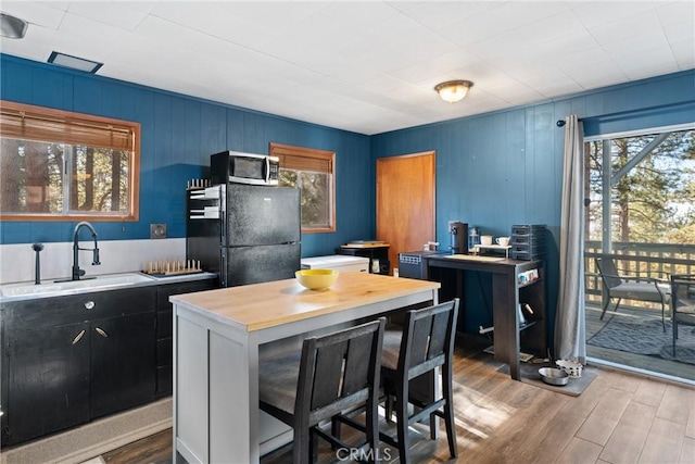 kitchen featuring sink, a breakfast bar, wood-type flooring, a kitchen island, and black fridge