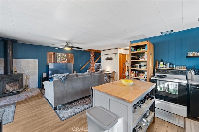 kitchen featuring light hardwood / wood-style flooring, ceiling fan, electric range oven, a healthy amount of sunlight, and a wood stove