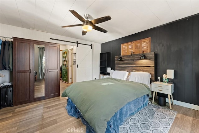 bedroom with a barn door, wood walls, ceiling fan, and light hardwood / wood-style floors