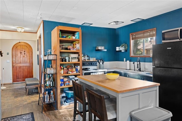 kitchen with sink, black refrigerator, a kitchen bar, white range with electric stovetop, and a kitchen island