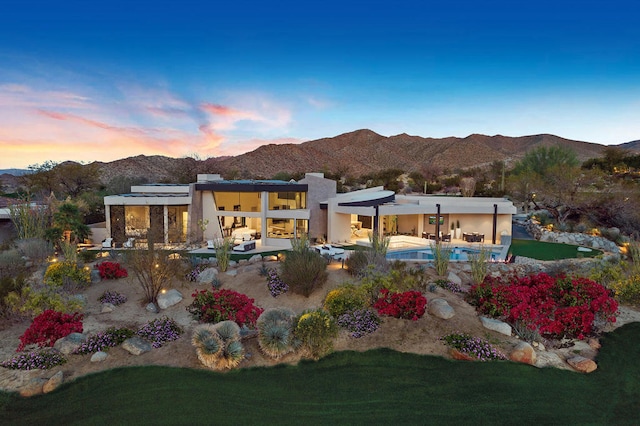 back house at dusk with a yard, a mountain view, and a patio