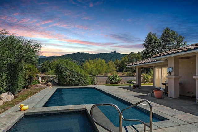 pool at dusk with an in ground hot tub, a mountain view, and a patio