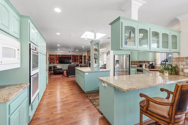 kitchen with sink, light stone counters, ornamental molding, kitchen peninsula, and stainless steel appliances